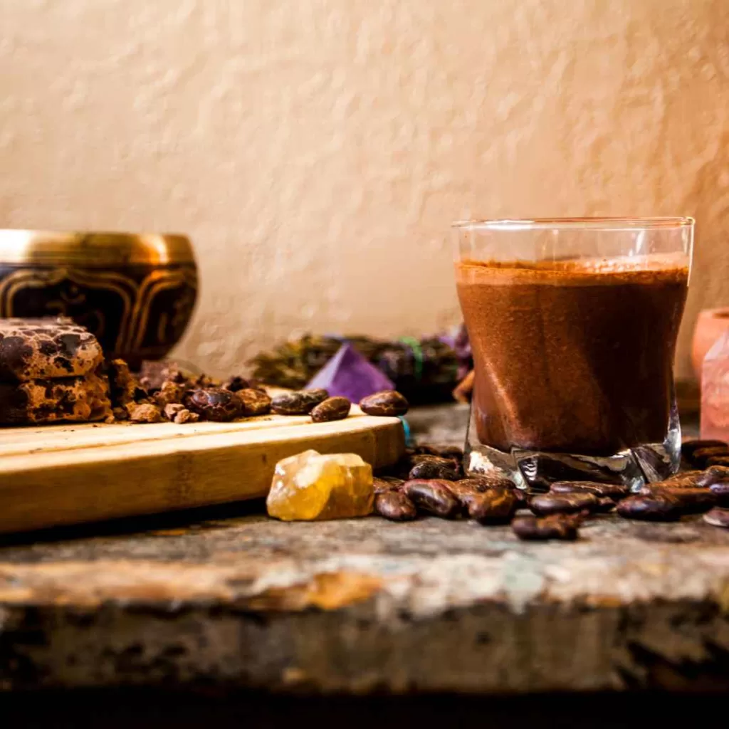 A beautifully arranged flat lay of organic ceremonial sipping cacao in a traditional ceramic cup, surrounded by cacao beans, spices, and a rustic textile.
